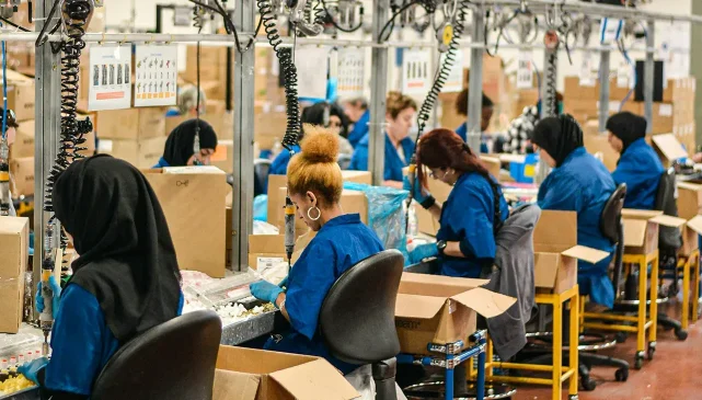 Female workers in a textile factory, sat at sewing machines.