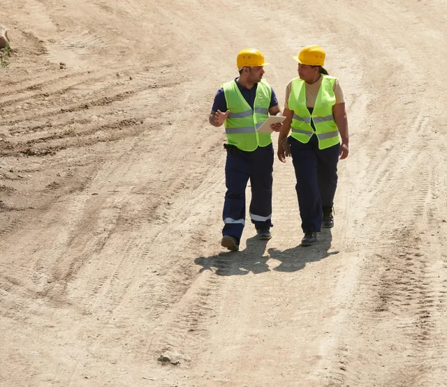 Two workers in hardhats and hi-vis walking through a construction site