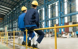 Two male factory workers sat talking to each other