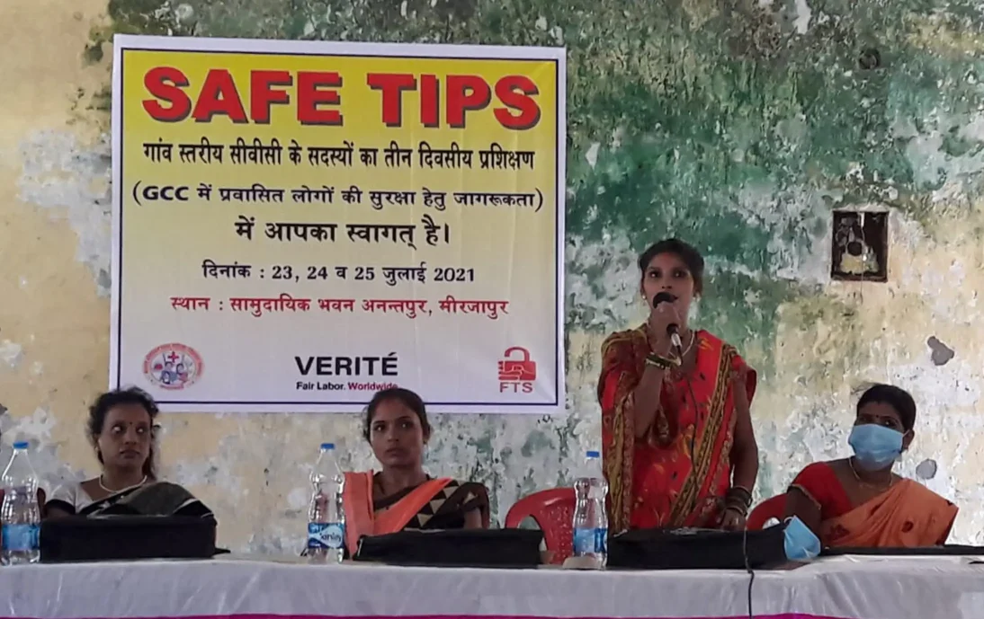Migrant worker community guidance in India: A woman speaking into a microphone in front of a SAFE TIPS banner